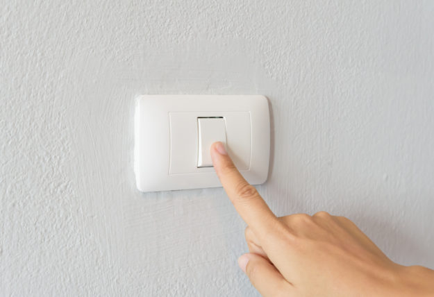 Close up of woman finger turning on light switch with white bac