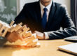 Person in a dark suit and blue tie plays a wooden Jenga tower on a office desk, hands steadying blocks.