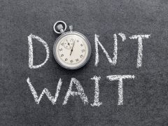 Stopwatch resting on a dark chalkboard with the words “DON'T WAIT” written in white chalk behind it.