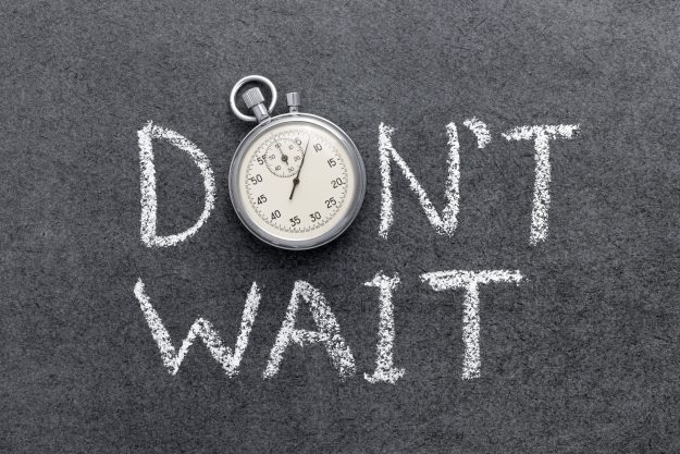Stopwatch resting on a dark chalkboard with the words “DON'T WAIT” written in white chalk behind it.